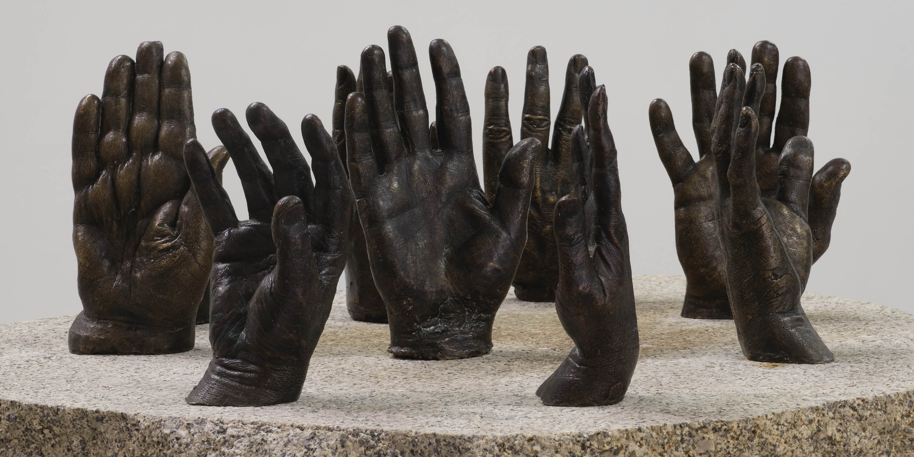 Installation shot of Raymond Watson's work 'Hands of History'. Assortment of bronze cast hands arrange on a stone plinth.